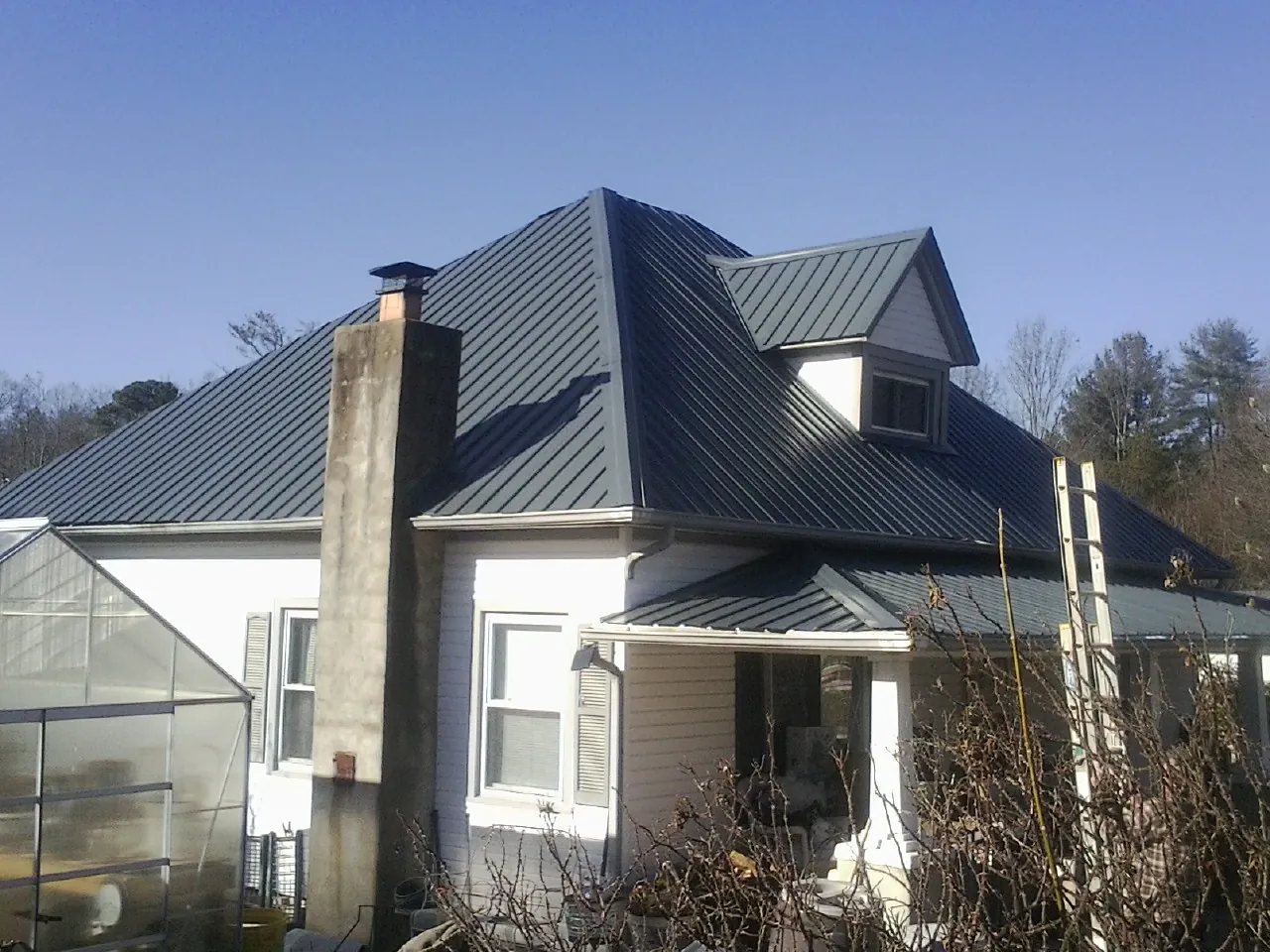 Dark blue standing seam metal roof on a white farmhouse with dormer — Slate & Tile Roof Repair by Roofing Brothers in Gibsonville