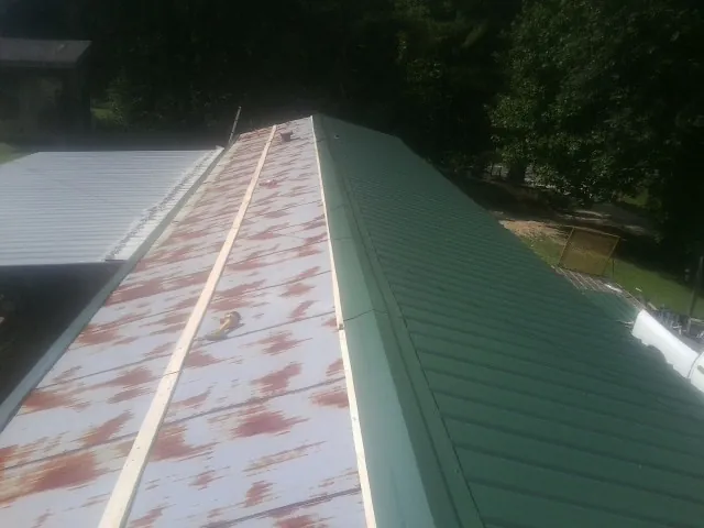Old rusted panels beside newly installed green metal roofing — Wind Damage Roof Repair by Roofing Brothers in Gibsonville