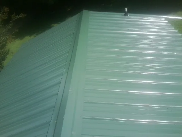 New green metal panels meeting at the ridge of a roof — Flat Roof Repair work by our crew in Gibsonville
