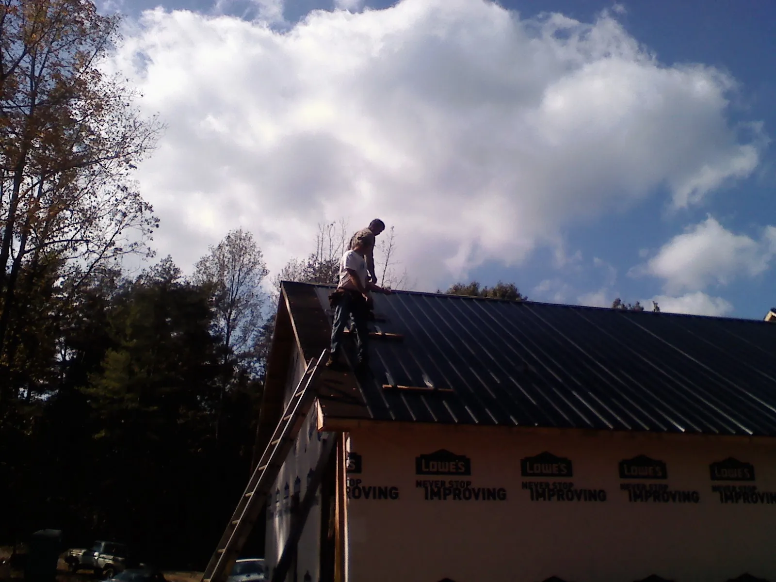 Roofer fastening dark metal panels high against a cloudy sky, from a Roof Inspection job in Gibsonville