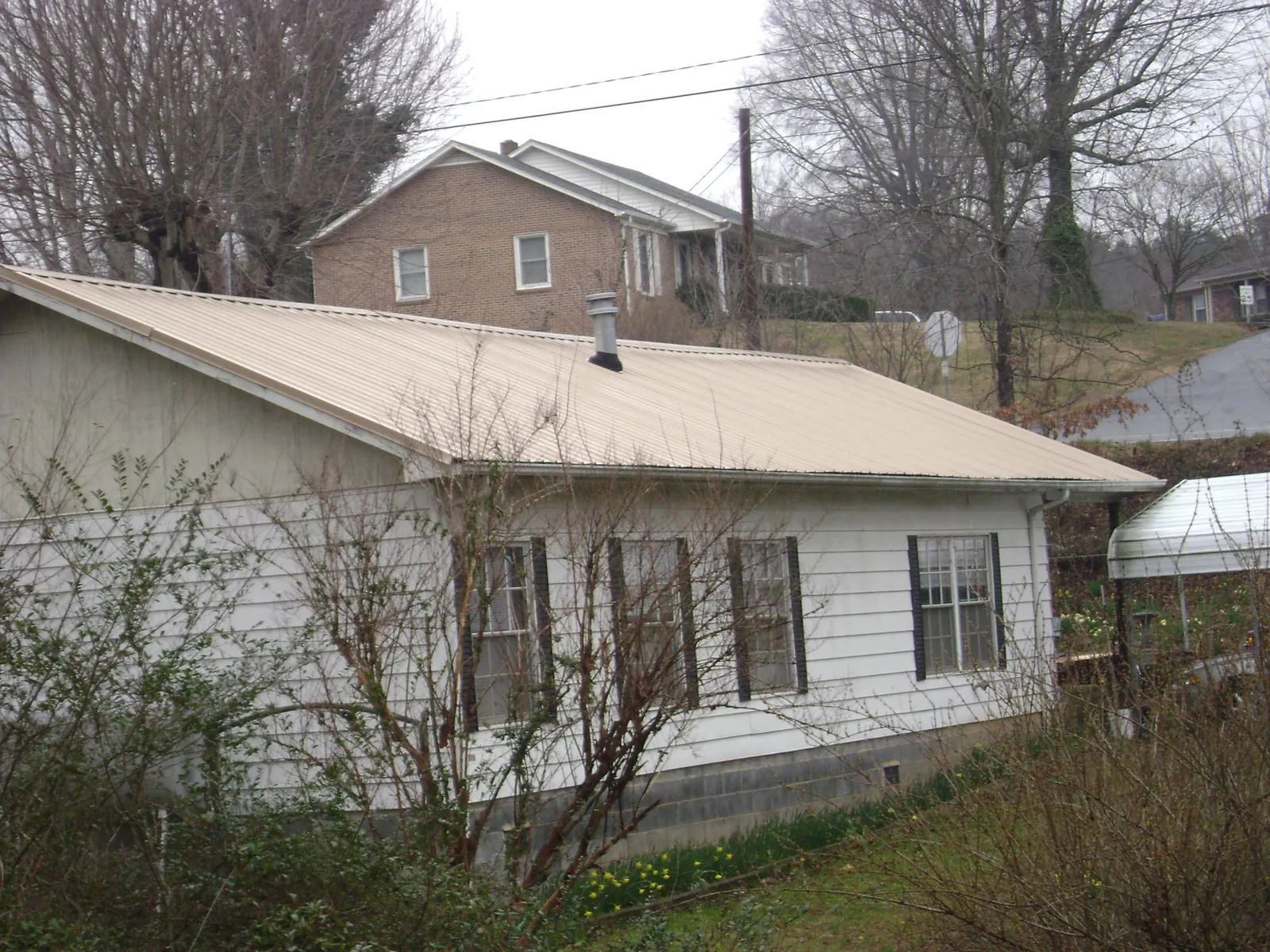 Tan metal roof on a white sided house set into a hillside in Gibsonville