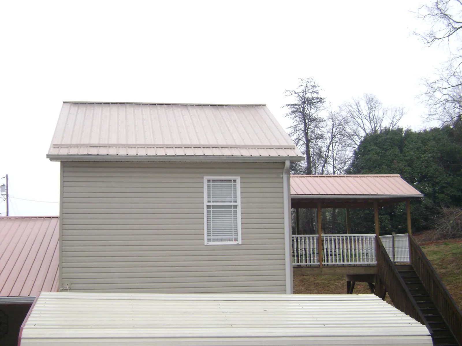 Tan metal roofs on a two story addition and attached porch, from a Roof Replacement job in Gibsonville